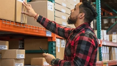 A person holding a phone in a warehouse near a stack of boxes.