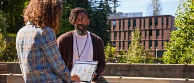 Eine Person, die einen Laptop hält, spricht mit einer anderen Person.